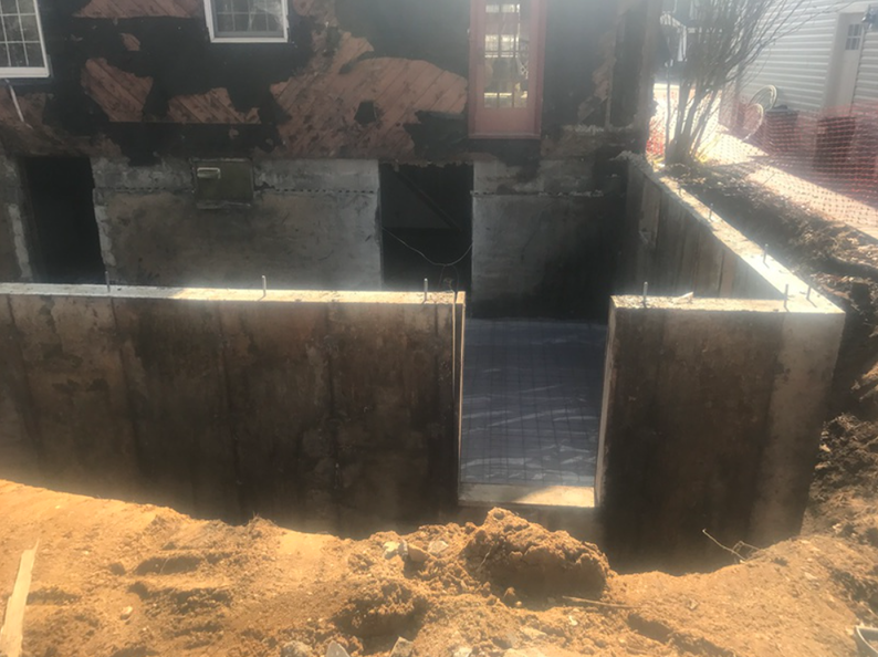 Construction site with a new concrete foundation being built beneath an old building's doorway.