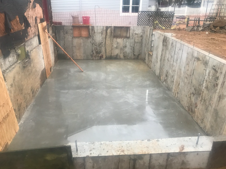 Concrete slab poured in a rectangular, walled-in area, with wooden formwork and walls.