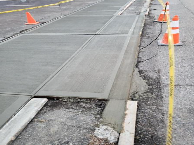Freshly poured concrete sidewalk with safety cones and caution tape.
