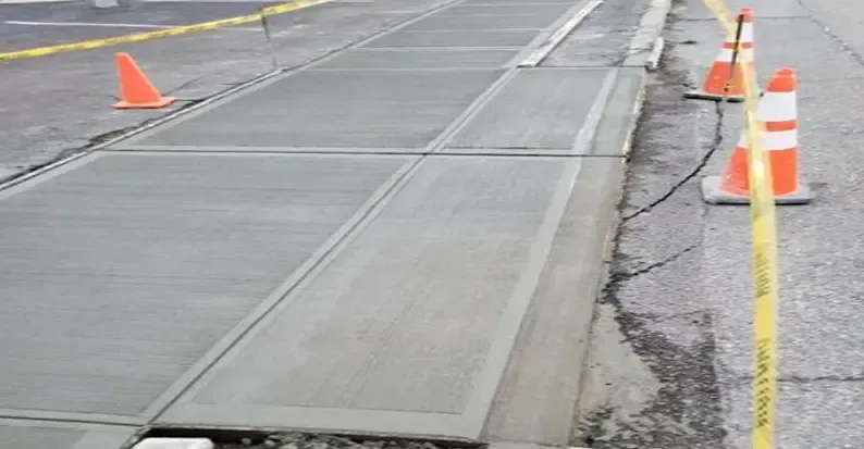 Newly poured concrete sidewalk with safety cones and caution tape.