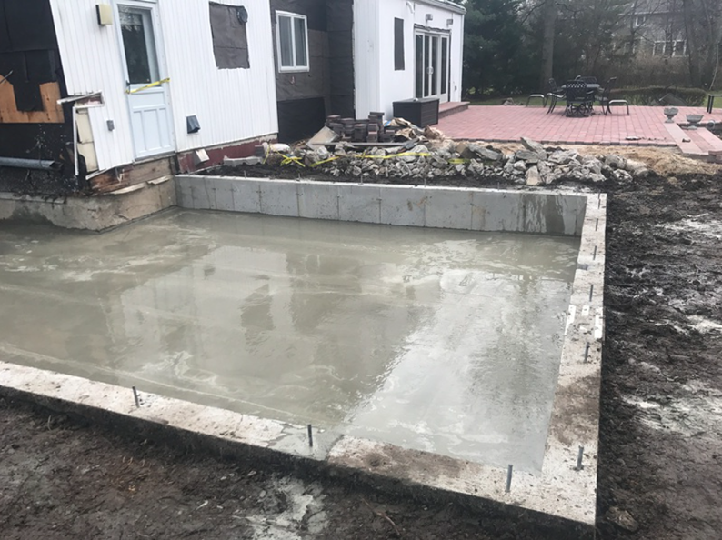 Newly poured concrete patio with low concrete walls, next to a white house and a red brick patio.