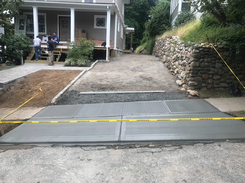 Newly poured concrete driveway with caution tape in front of a light brown house.