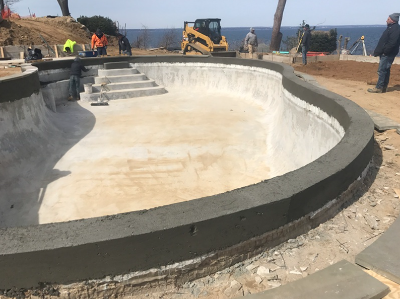 Construction of an in-ground pool with concrete coping, stairs, and surrounding construction site.
