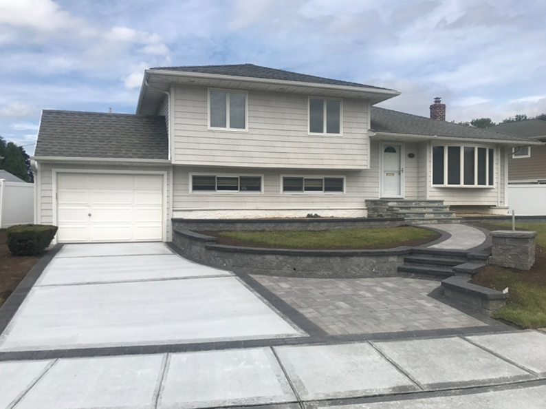 Two-story house with light siding, attached garage, concrete driveway, and a paver walkway.