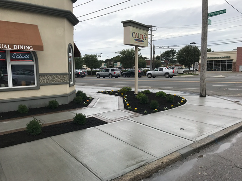 Corner sidewalk with Calvino Restaurant sign, landscaping, and vehicles on the street.