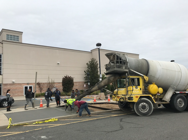 Construction workers pouring cement from a yellow truck in front of a beige building.