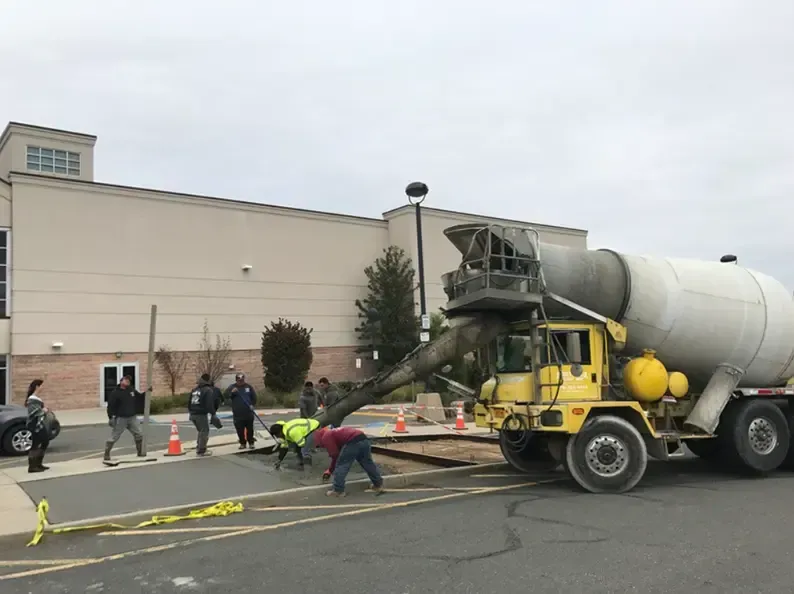Yellow cement truck pouring concrete onto a sidewalk; construction workers are present.