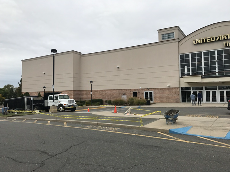 Exterior view of a United Artists movie theater with construction activity; a truck, caution tape, and construction materials are visible.