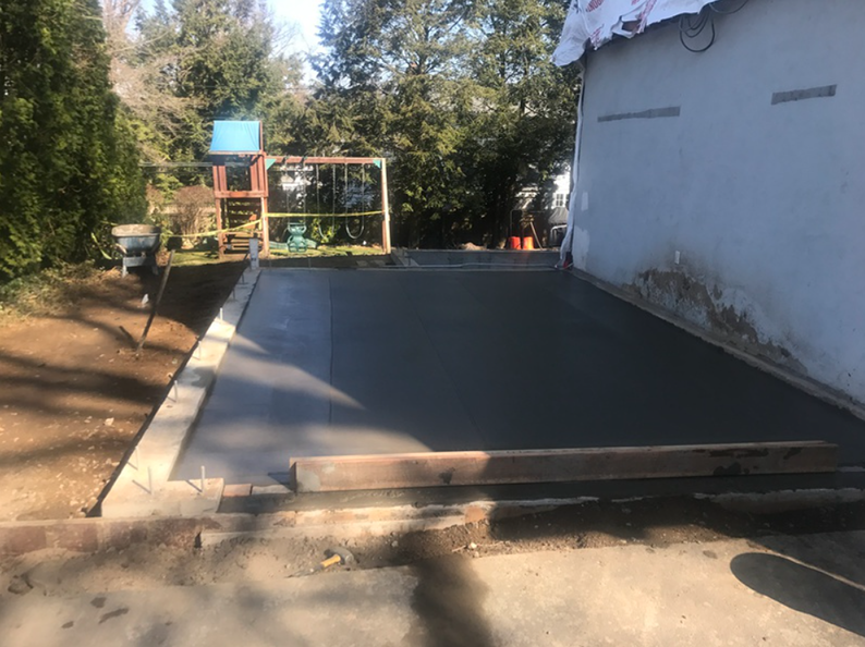 Freshly poured concrete patio next to a building and a kids' play structure.