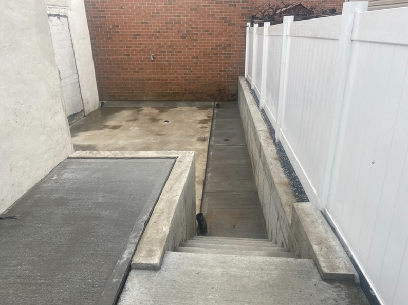 Concrete basement steps leading downwards, bordered by a white fence on one side.