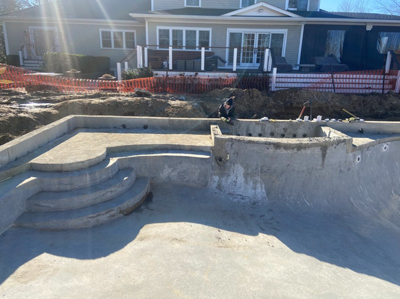 Concrete pool under construction with steps and a raised spa area; a worker is present.