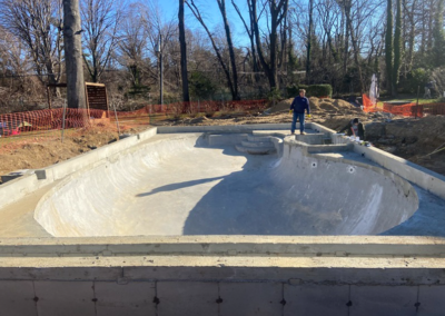 Concrete skate bowl under construction; a person stands on the coping. Sunny outdoor setting.