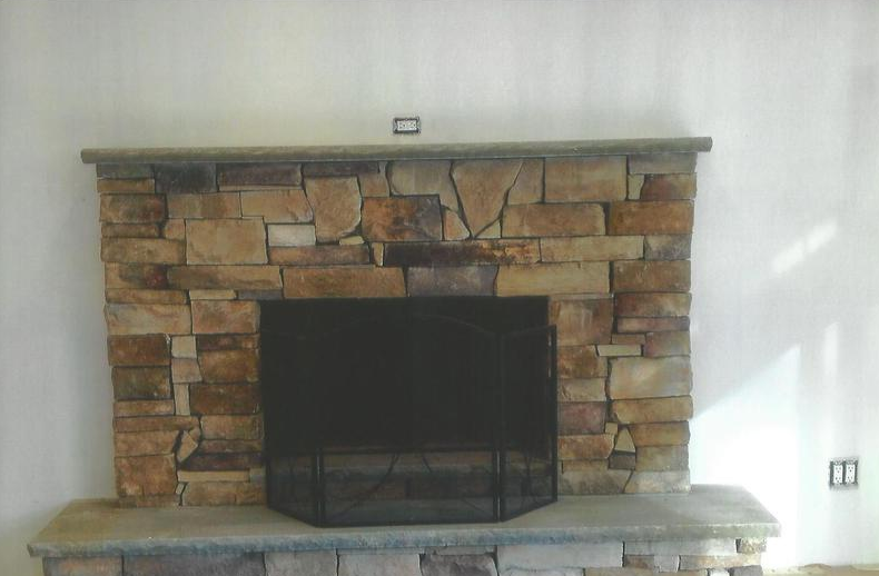 Stone fireplace with a black screen against a white wall.