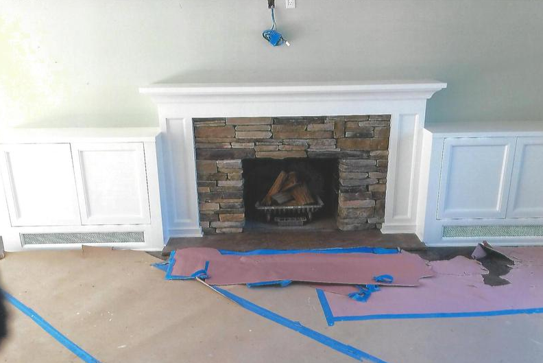 Fireplace with stone surround, white mantel, and built-in white cabinets on either side. The floor is covered in brown paper.