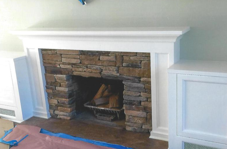 White-trimmed fireplace with stone surround and wood.
