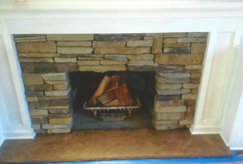 Stone fireplace with burning logs, dark interior, white trim.