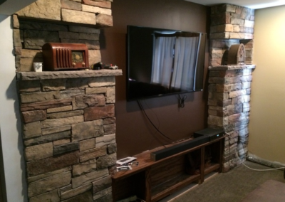 Stone-framed TV wall with a TV, sound bar, and a vintage radio. Brown and beige color scheme.