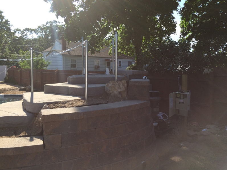 Stone steps with a metal railing in a backyard, leading up to a raised patio.