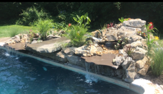 Waterfall feature cascading into a blue swimming pool, surrounded by rocks and green plants.
