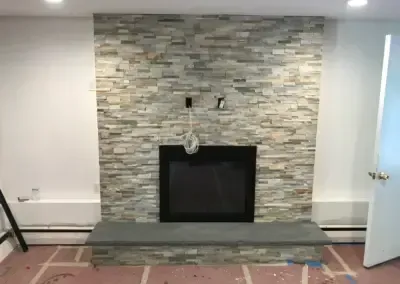 Fireplace with stone facade, dark firebox, and gray hearth in a room with unfinished flooring.