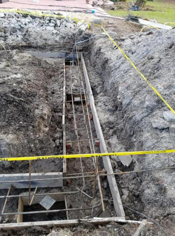 Construction site with excavated trench; rebar framework prepared for concrete foundation.