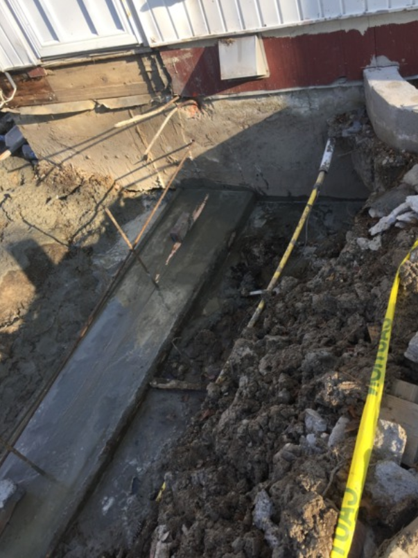 Concrete work in progress beside a building foundation. A yellow tape marks off the area.