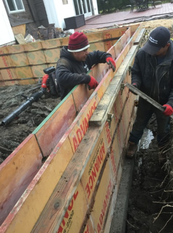 Two construction workers building concrete forms, red gloves, outdoors.