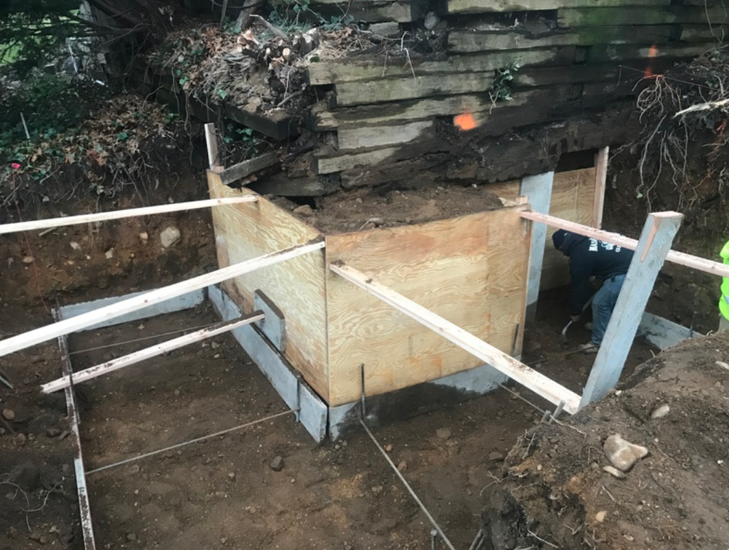 Construction of a concrete form with wooden supports in an outdoor setting. A worker is visible.