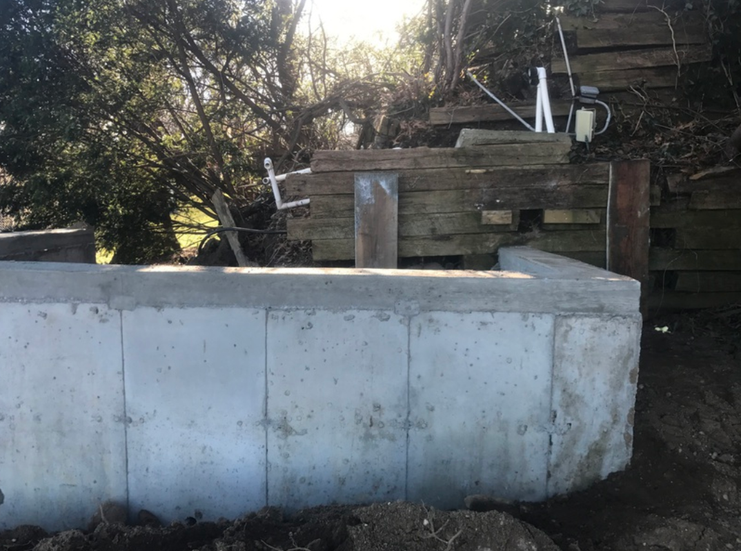 Concrete foundation wall beside a wooden retaining wall, in a natural outdoor setting.
