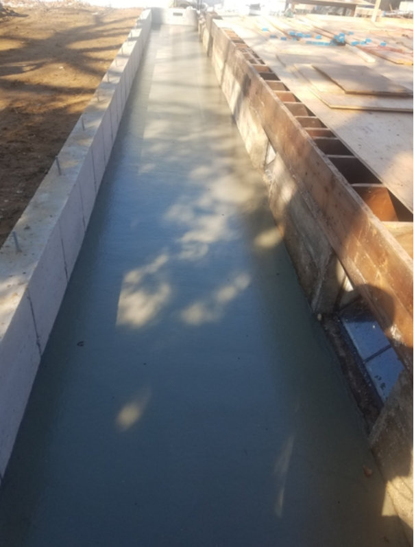 Concrete construction project with a long, rectangular channel filled with wet concrete.