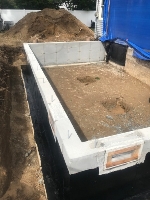Rectangular concrete structure being built, surrounded by dirt and black tarp. Construction site, outdoor.