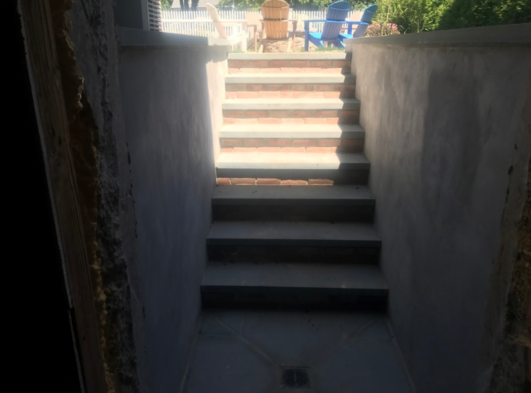 Concrete stairs leading from a dim interior up to a sunlit outdoor area with a view.