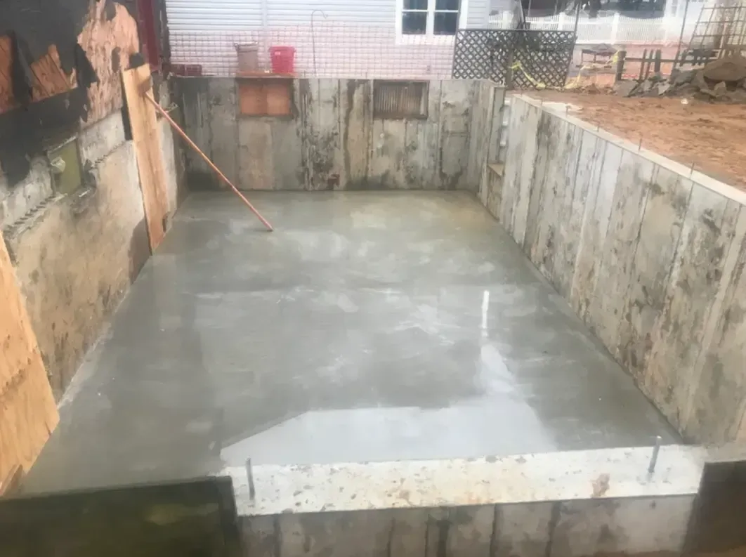 Concrete floor poured in a rectangular pit, surrounded by wooden and concrete walls; outdoor setting.