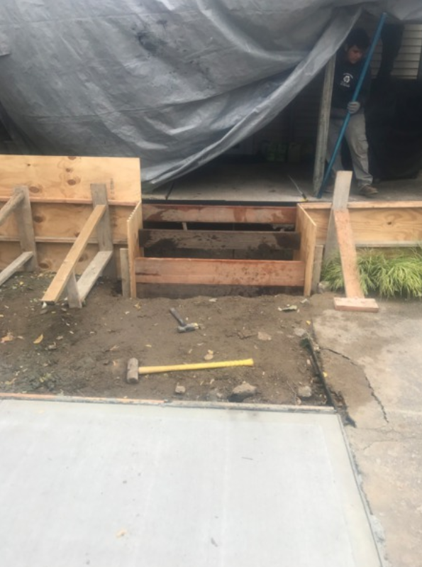 Wooden forms for concrete steps being built outside. A worker is visible. Ground level shot.
