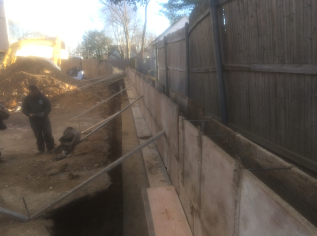 Construction site with worker, retaining wall being built next to a wooden fence.