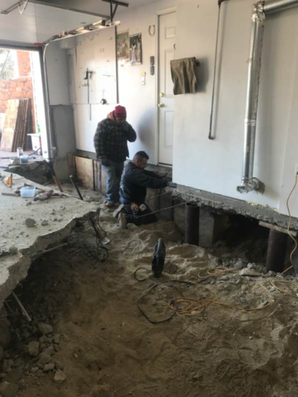 Two men working in a garage under construction, removing concrete from the floor.
