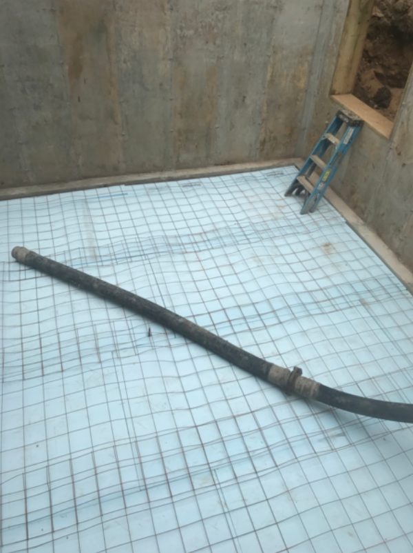 Inside a concrete room, a construction site; rebar grid on blue foam, hose, ladder in the corner.