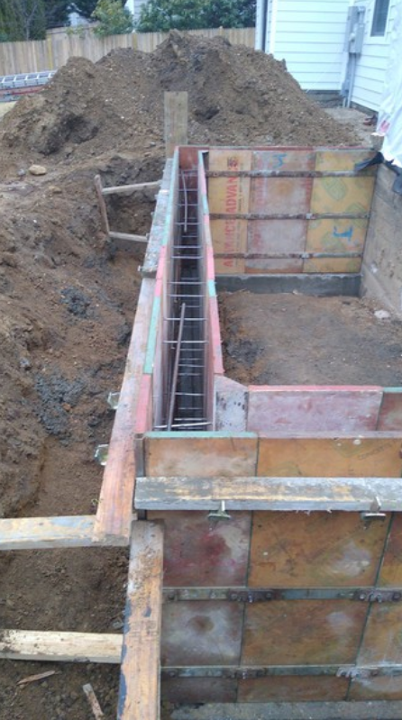 Foundation construction site with wooden forms, rebar, and a pile of dirt.