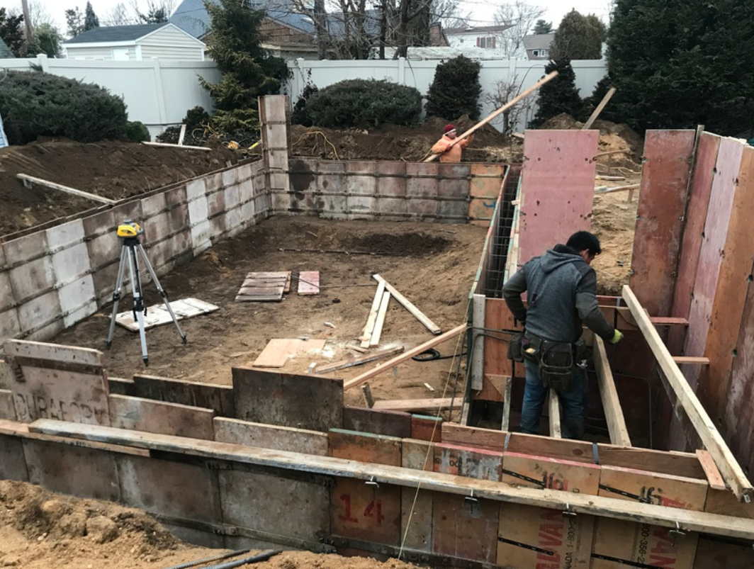 Construction site: Worker building forms for concrete. Ground is excavated, with cinder block walls.