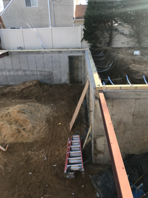Construction site with concrete foundation, dirt, ladder, and blue pipes.