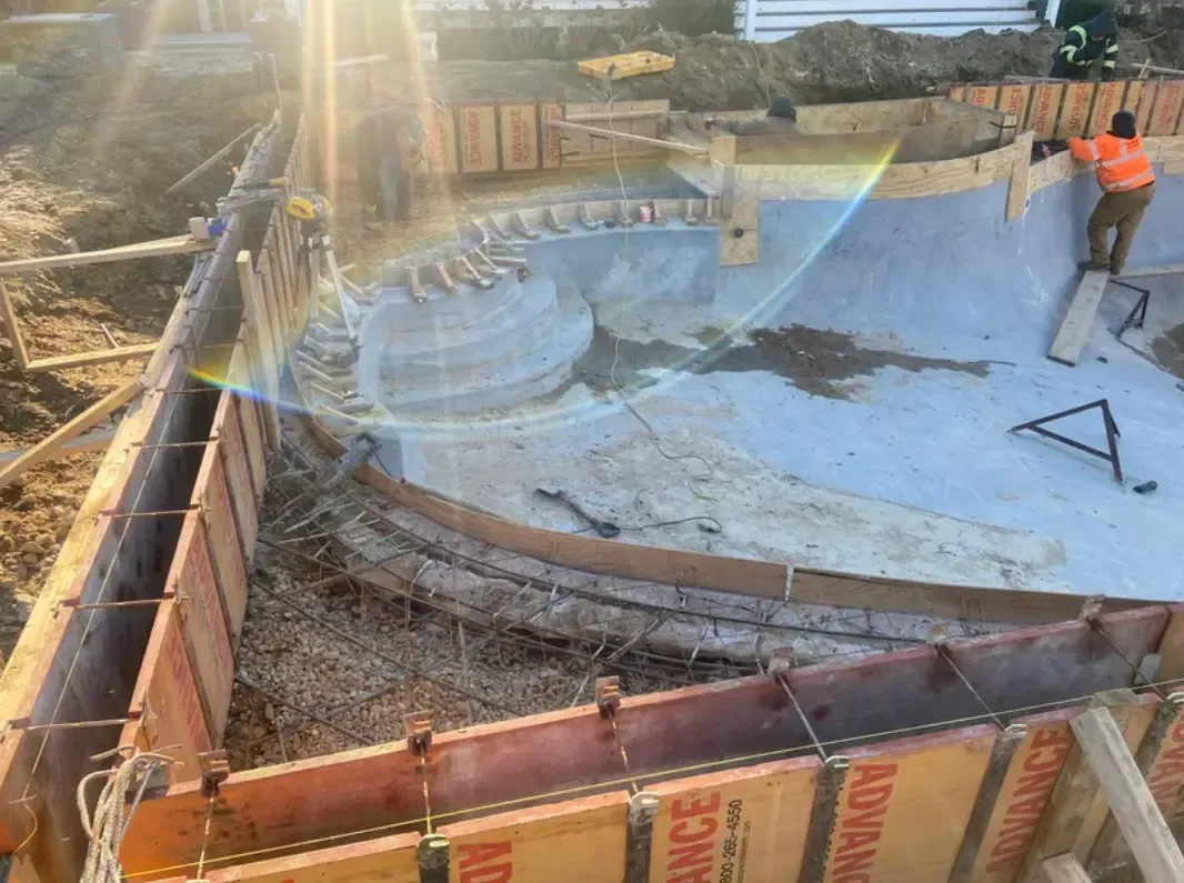 Construction site of a pool; workers are building the concrete structure with wood framing.