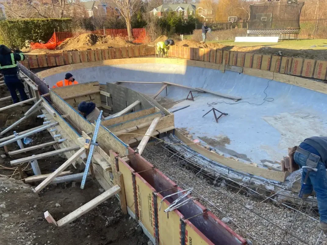Construction of a pool with wooden forms, concrete, and workers in an outdoor setting.
