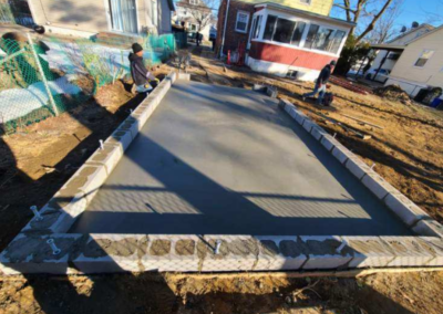 Concrete slab framed with gray blocks in a yard; two workers tending to it.