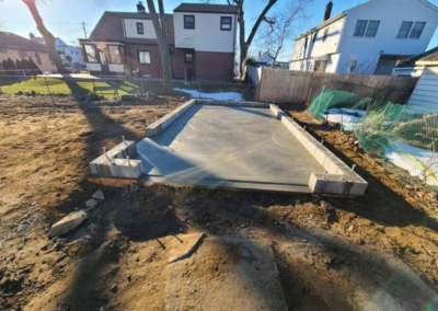 A concrete foundation with cinder block sides on a dirt lot, in a residential backyard.