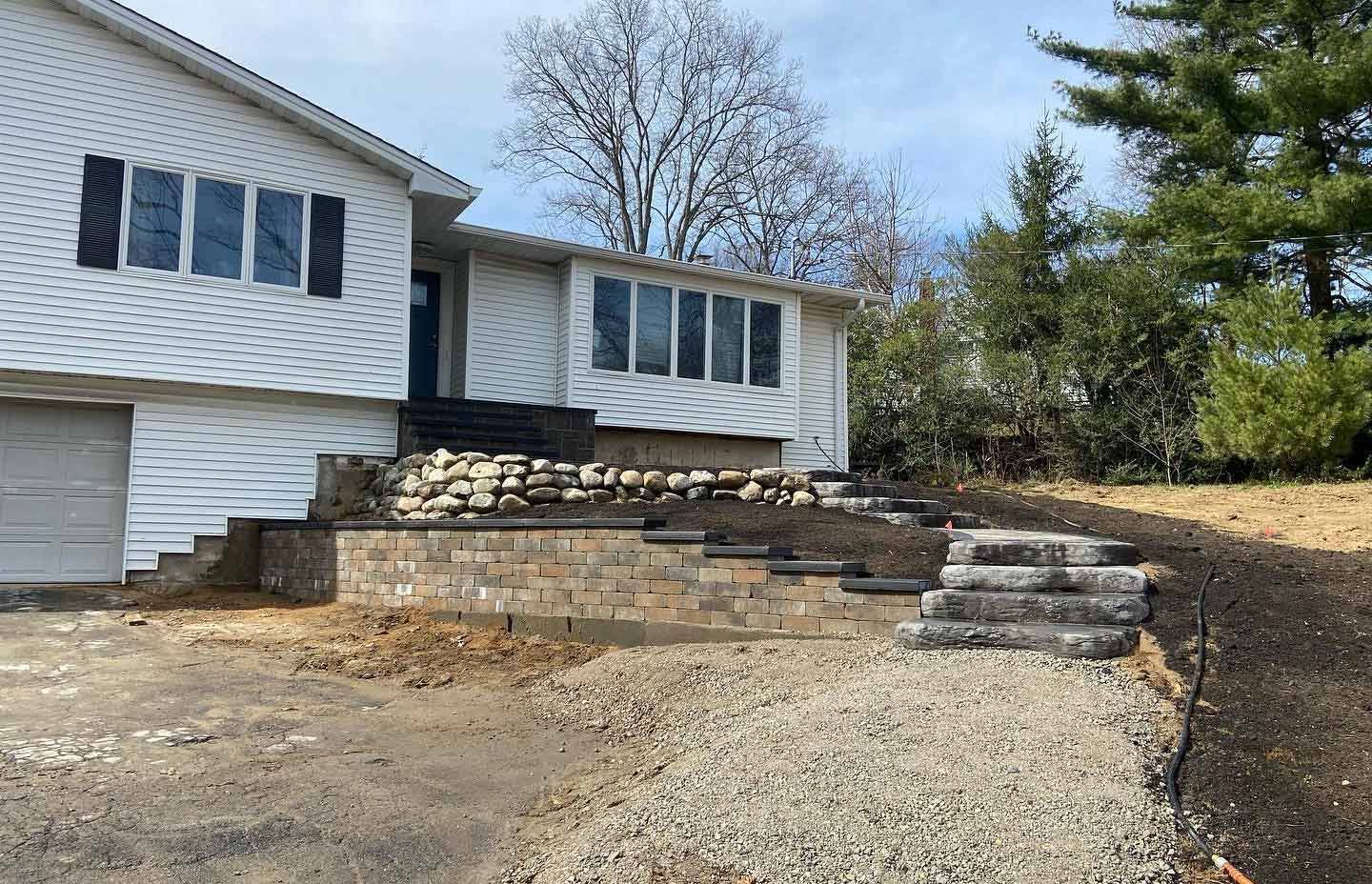 White house with stone steps leading up to the front door. Gravel driveway.