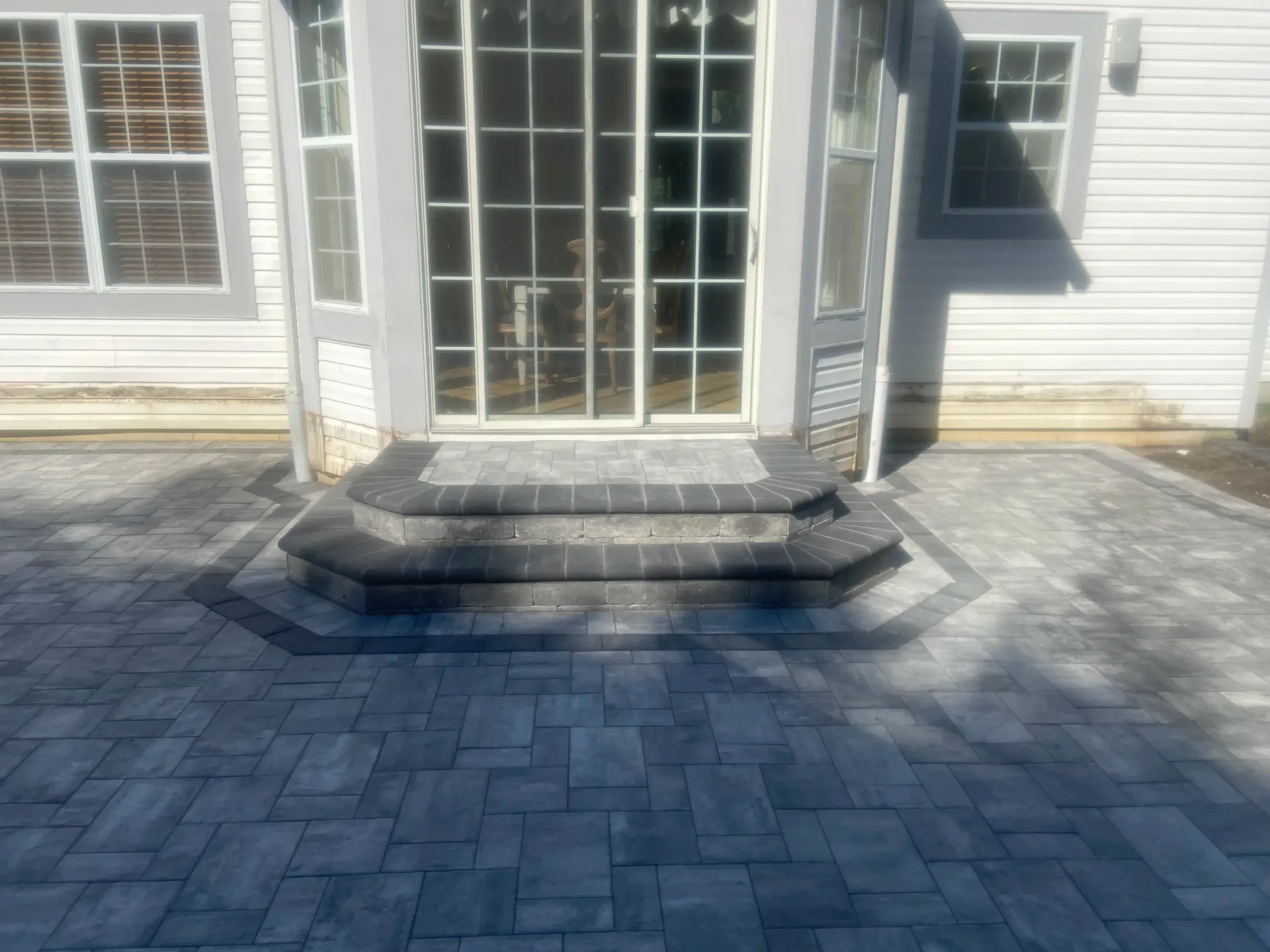Patio with brick steps leading to a sliding glass door. Gray pavers and white siding.