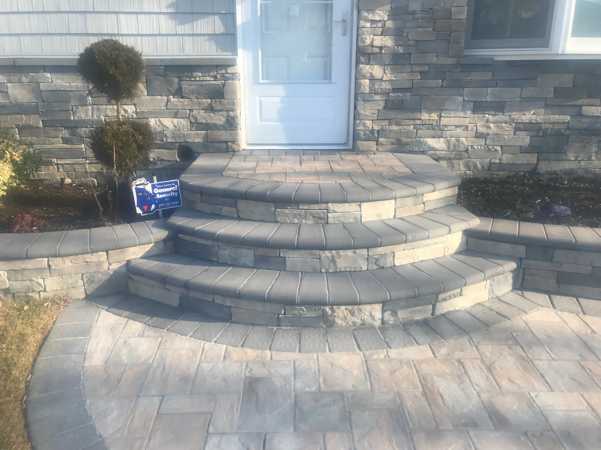 Stone steps lead to a white door, with stone veneer walls and a paved walkway.