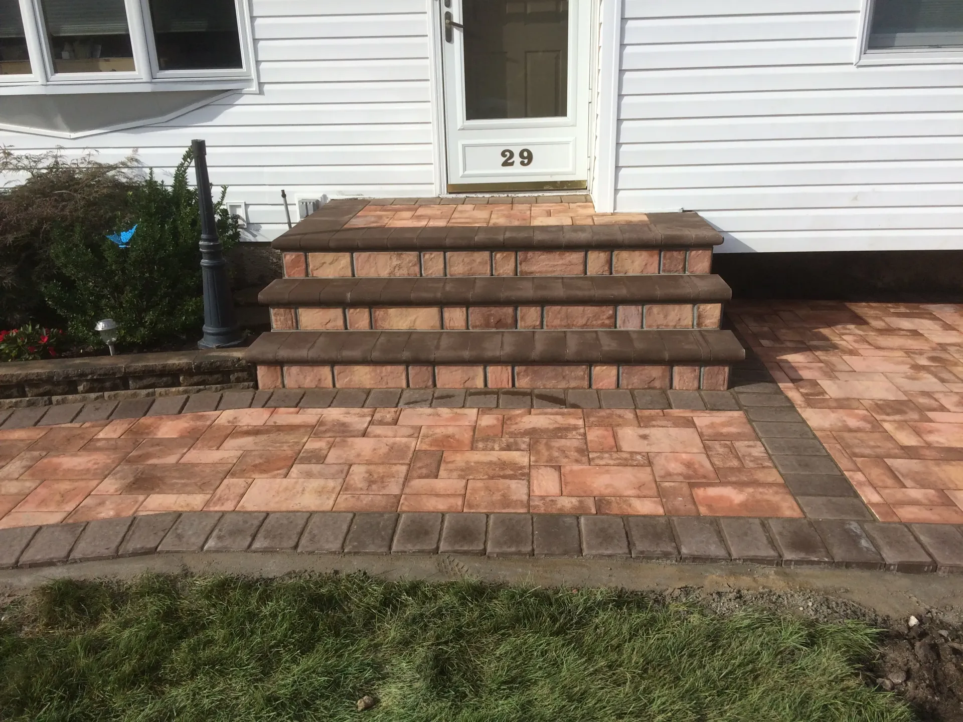 Brick steps leading to a white door, bordered by matching brick walkway. Green grass in foreground.