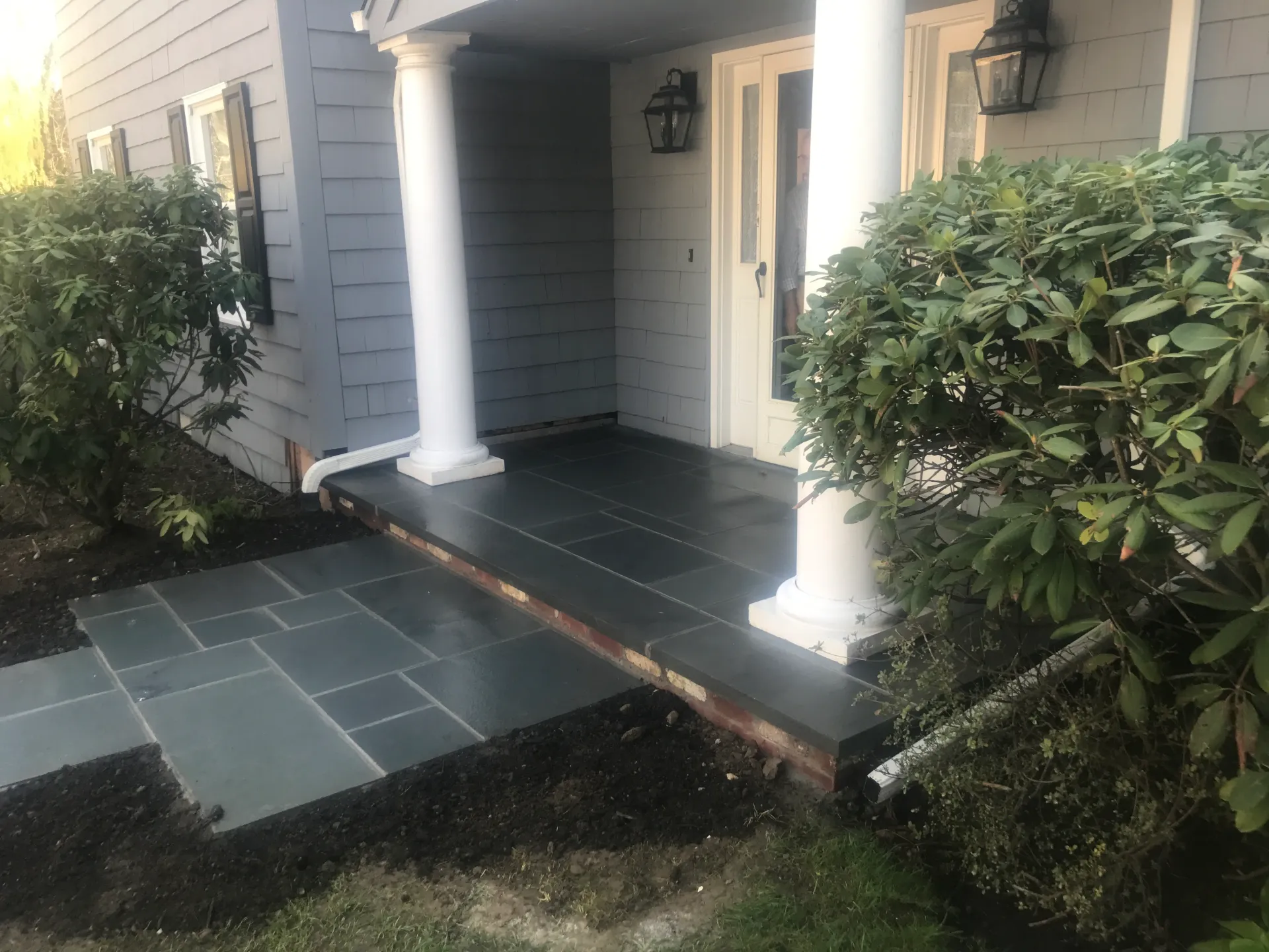 Slate patio and walkway leading to a house entrance, surrounded by bushes and a white column.