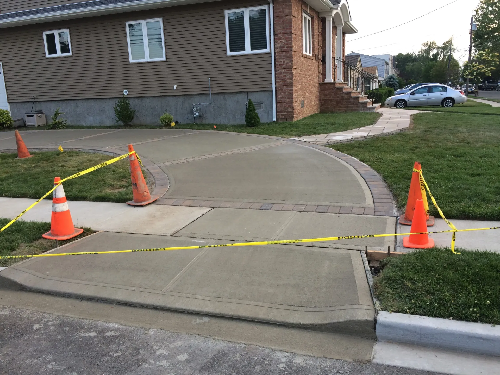 Freshly poured concrete sidewalk with cones and caution tape in front of a house.